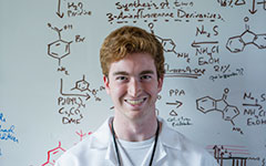 Smiling student standing in front of a white board with chemistry content on the board.