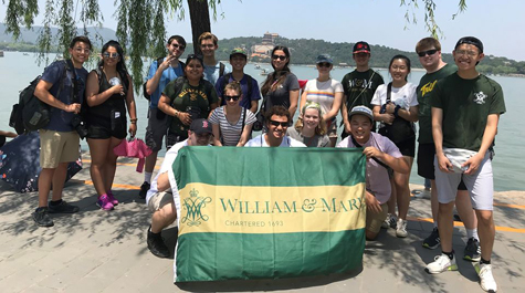 Students pose for a photo together on a beach and holding a William & Mary flag