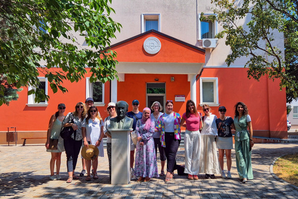ABC Project students and faculty standing beside a large head statue with a bright orange building behind them.
