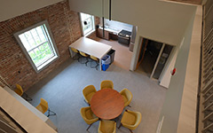 A large lounge with kitchen area featuring exposed brick, peninsula island, seating areas with chairs, dining table and modern decor