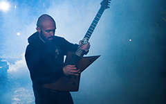 A guitarist in a dark smoke-filled room playing a Gibson Explorer-style electric guitar