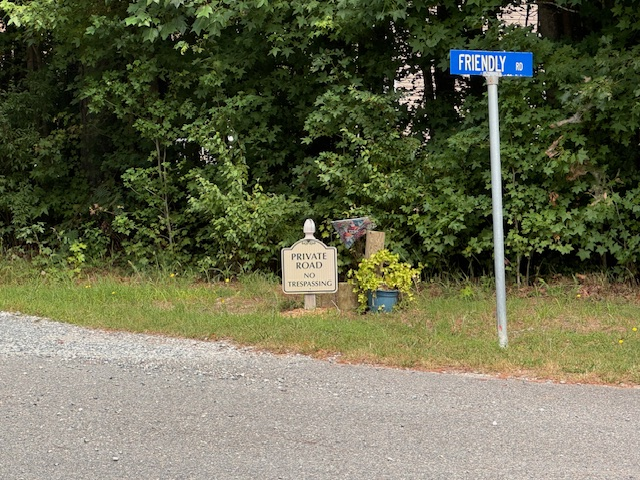 Conflicting signs on the road. One says "Friendly Road" and the other says "Private road"