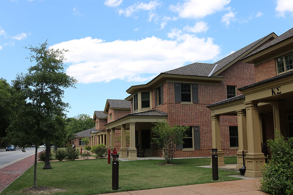 Brick fraternity houses in a row along the street with brick sidewalks, trees and shrubs