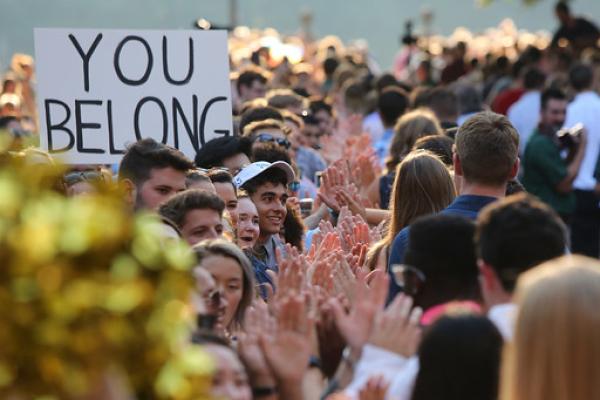 A crowd of people from campus community greet first-year students with a 'You Belong' sign.