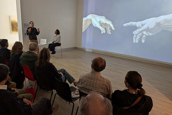 Two people discussing and presenting to a room of students and faculty with a projection of a closeup of Michelangelo's work behind them