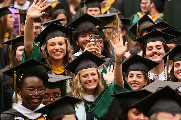 A group of graduates smiling and waving.