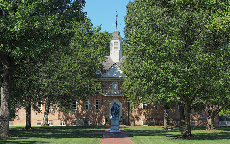 View of the Sir Christopher Wren Building with Lord Botetourt statue and large trees in front on a sunny, blue sky day.