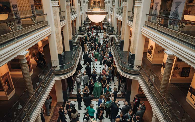 A For the Bold celebration event with people congregated and talking in the atrium of a museum