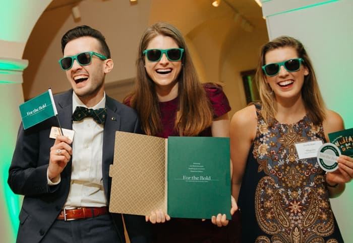 Three smiling people celebrating in green sunglasses holding green and gold campaign materials