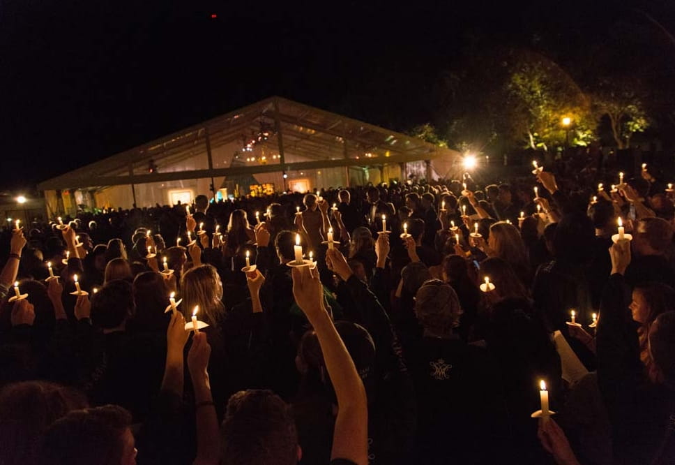 Large crowd of people in formal attire holding up ceremonial burning candles at night in the Sunken Garden