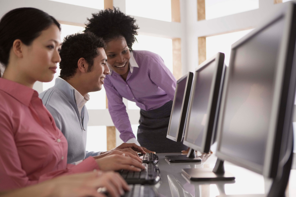 A trainer helps two people sitting at desktop computers.
